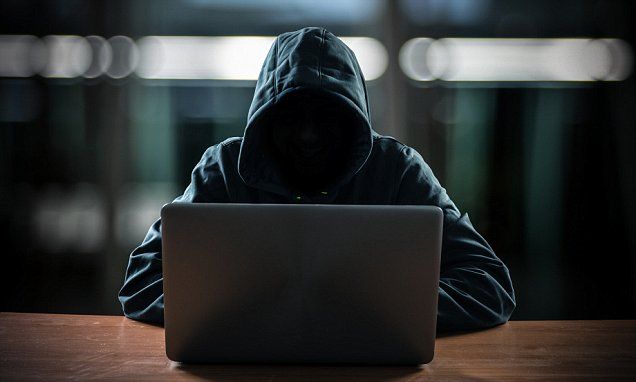 Persona encapuchada en la oscuridad frente a un computador, representando a un estafador digital.