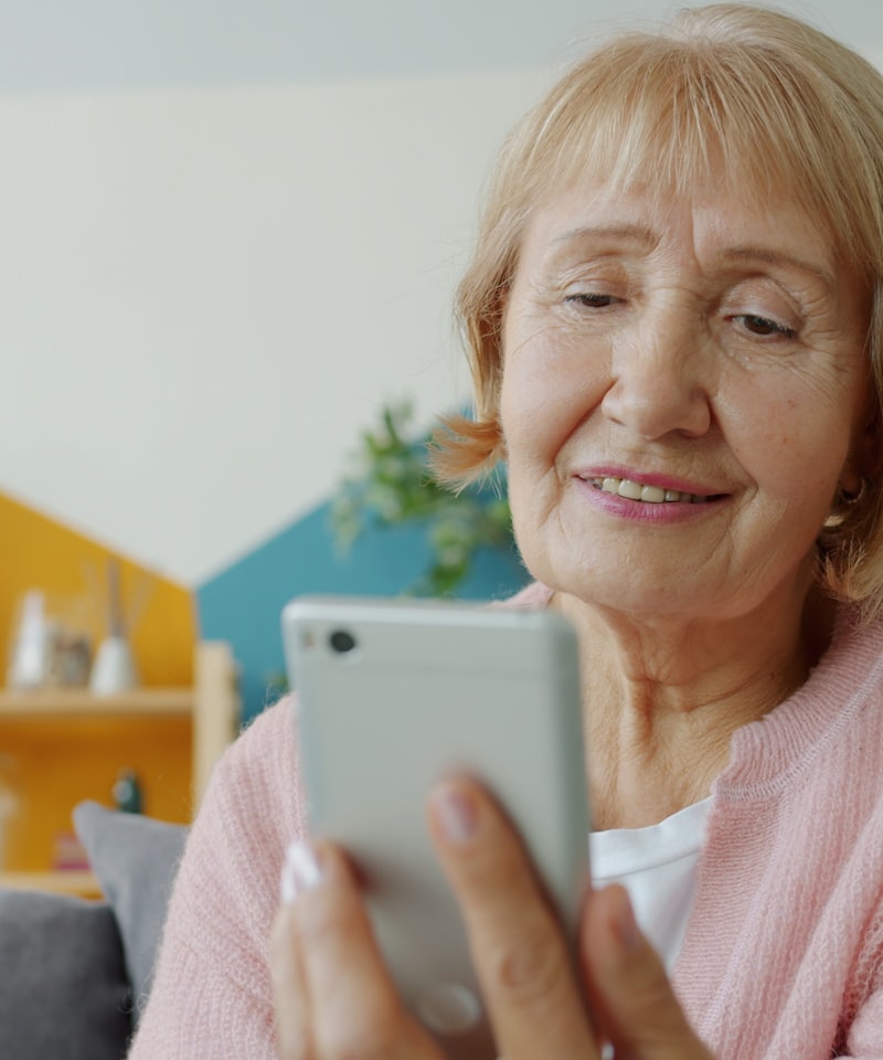 Persona mayor sonriendo mientras usa su teléfono celular con tranquilidad.